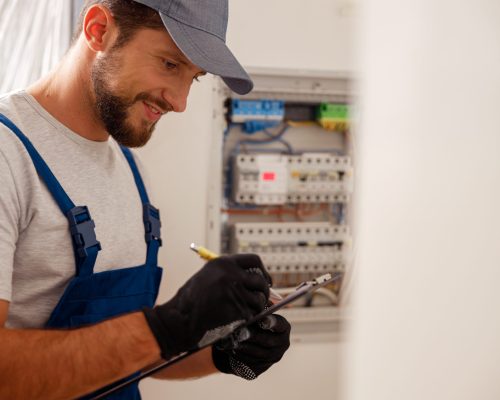 Busy electrical technician writing on a clipboard the data collected on a residential electric panel. Maintenance, occupation, safety concept